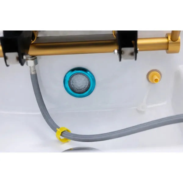 Detailansicht einer Kopfspa-Liege: grauer Schlauch, blauer Abflussring und weiße Oberfläche.