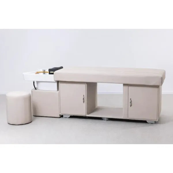 Beige Kopfspa-Liege mit Keramik-Waschbecken, Stauraum-Unterschrank und Hocker im Spa-Setup.