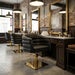 Schwarzer hydraulischer Friseurstuhl mit Armlehnen und goldenem Gestell in einem modernen Barber Shop.