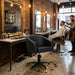 Schwarzer Friseurstuhl mit Armlehnen und hydraulischer Verstellung im rustikalen Barber-Shop Ambiente.