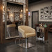 Beiger Friseurstuhl mit Armlehnen und Hydraulik im rustikalen Barbershop, neben stilvollem Tool-Cart und großen Spiegel.