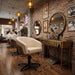 Creamefarbener Friseurstuhl mit Armlehnen vor vintage Barbershop-Interieur mit Messingspiegel und Backsteinwand.