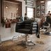 Schwarzer Friseurstuhl mit Armlehnen und Chromfuß im rustikalen Barbershop mit Spiegel und Holzboden.