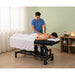 Electric massage table with 1 motor, height-adjustable; Massagebank Vital used by therapist to massage a client's back.