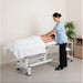 Therapist performs back massage on client on a height-adjustable electric massage bed in a spa setting.